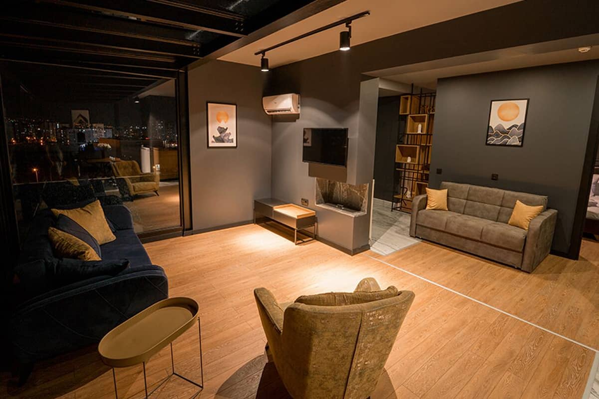 Ein modernes Wohnzimmer mit Sofa, Sessel und Couchtisch. Ein Kamin, ein Bücherregal und Kunstwerke schmücken die Wände.