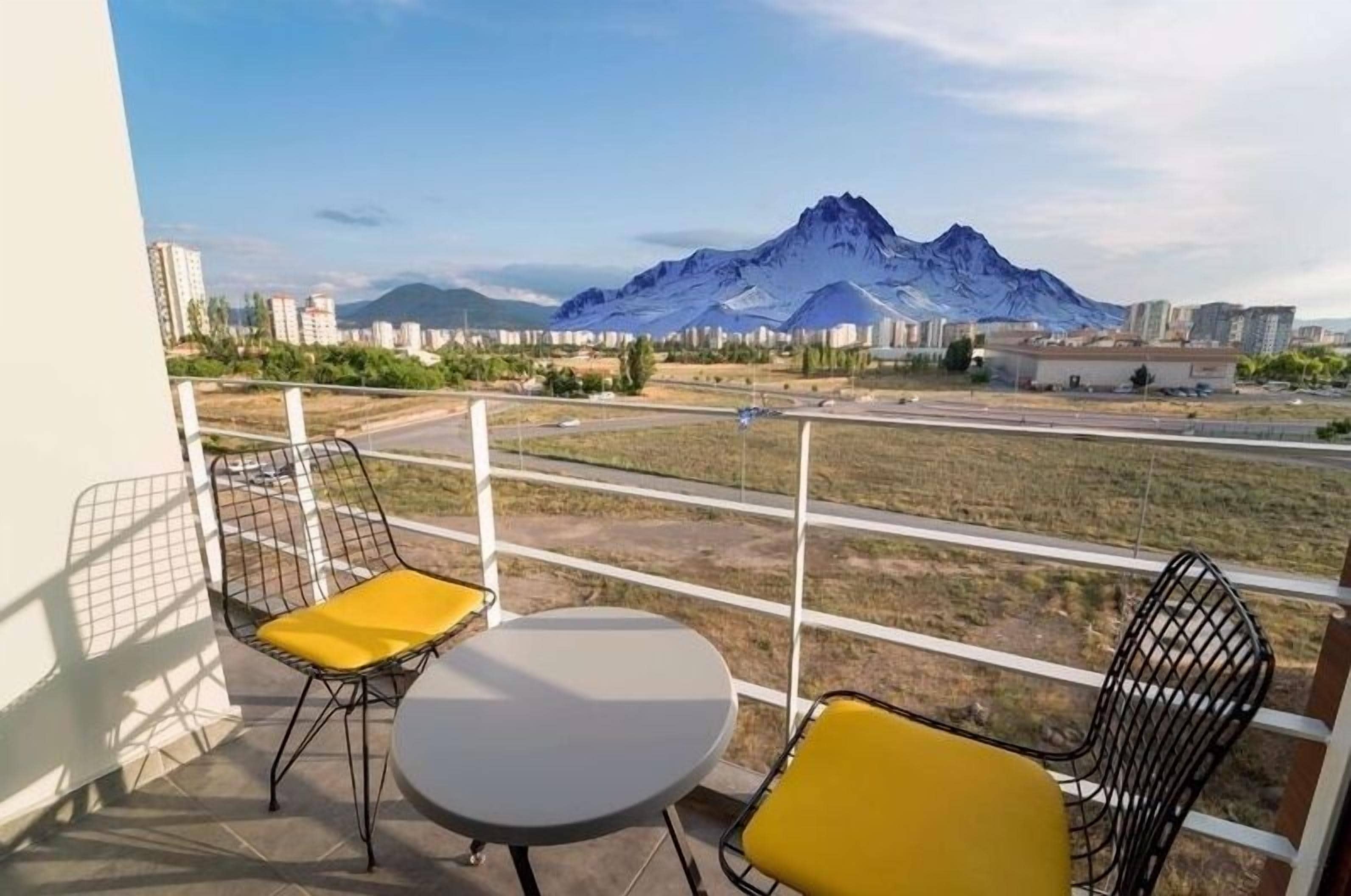 A balcony with two chairs and a table, overlooking a cityscape and a mountain.