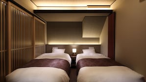 Ein Hotelzimmer mit zwei Betten, einem Nachttisch mit Lampe und einem verschiebbaren Shoji-Bildschirm.