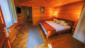 A wooden cabin room with a bed, a television, a door, and a window with curtains.