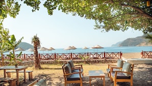 A beachside seating area with wooden furniture and thatched umbrellas, overlooking the sea.