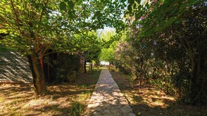 A stone pathway flanked by lush greenery and flowering plants, leading to a structure in the distance.