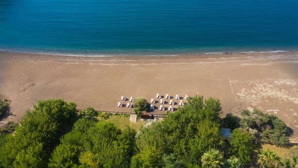An aerial view of a beach with a row of tents and a small building, surrounded by dense greenery.