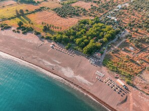 An aerial view of a beach with rows of sun loungers and a small building, surrounded by greenery and fields. - Eden Bungalows and Beach (Koycegiz)