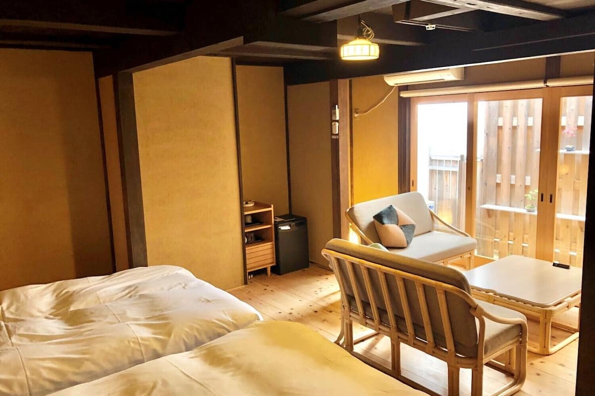 A room with two beds, a wooden chair, a small table, and a sliding door leading to an outdoor area.