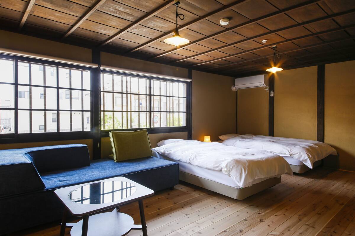 A room with a wooden ceiling, a sofa, a small table, and two beds.