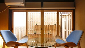 A room with a glass table and two blue chairs, wooden flooring, and a wooden fence outside. - Kariya Ryokan Q (Ako)