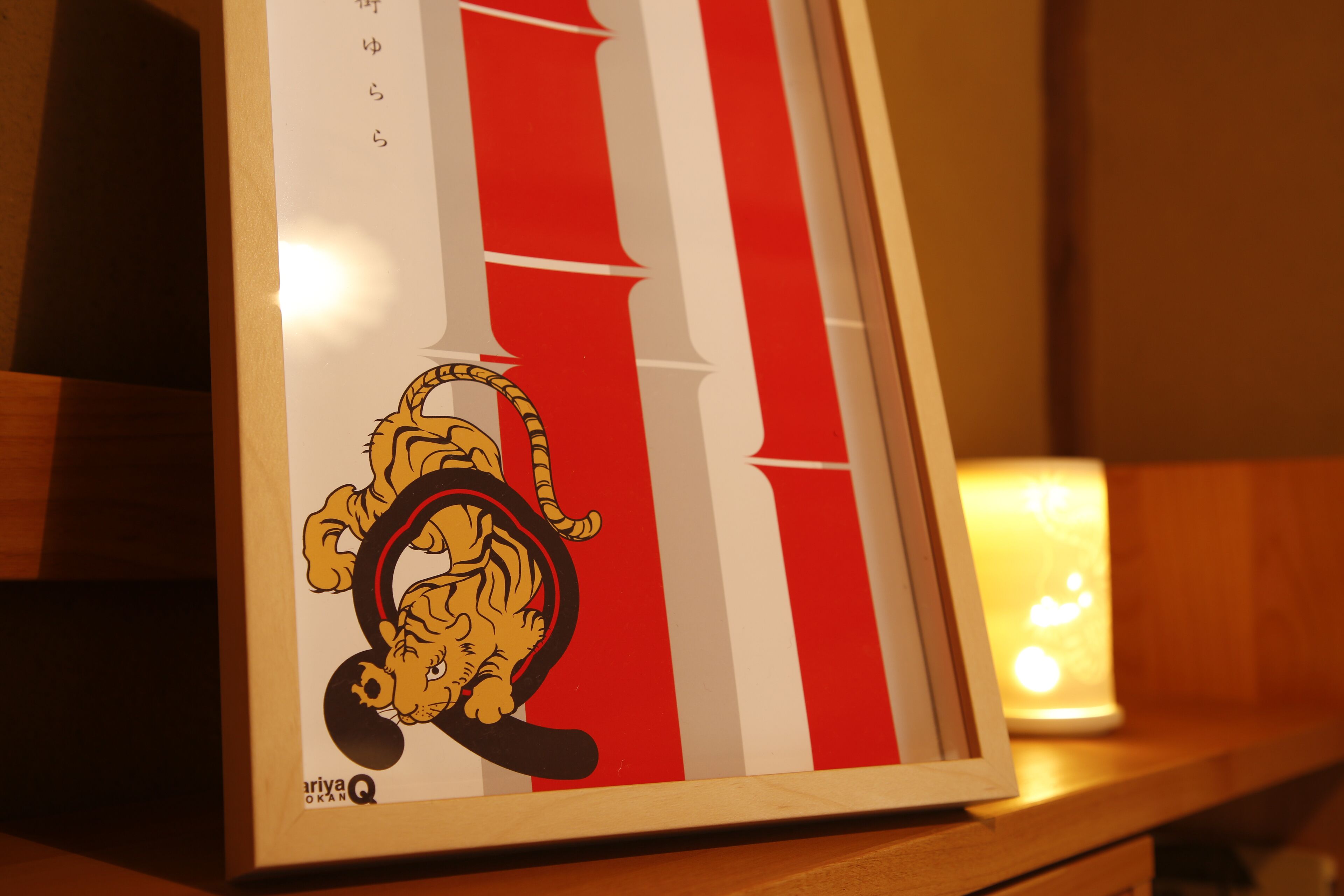 A framed picture of a cartoon tiger on a wooden surface with a candle in the background.