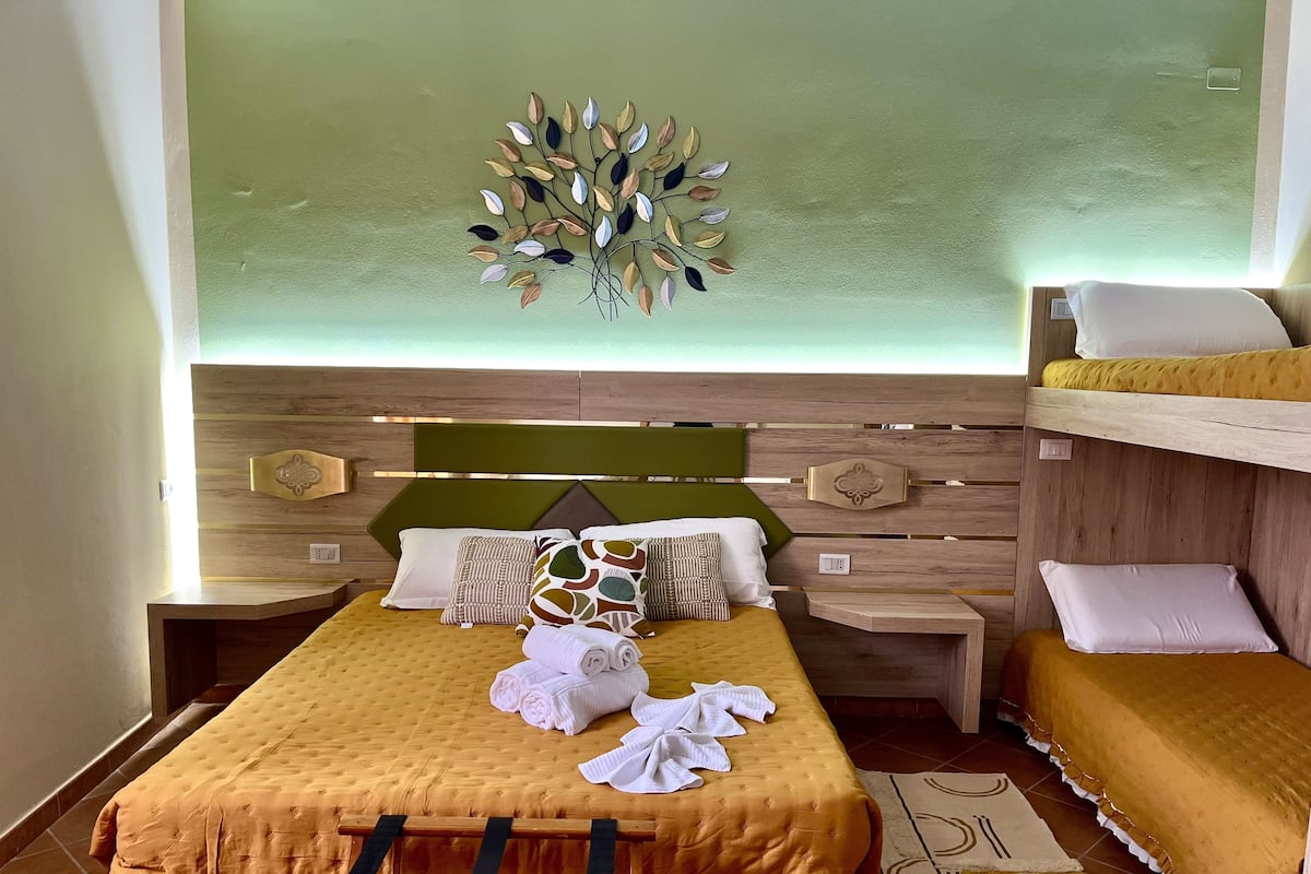 A hotel room with a bed, a bunk bed, a decorative wall piece, and a bedside table.