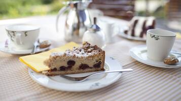 Ein Stück Kuchen auf einem Teller mit einem Löffel, einer Tasse und einer Kanne auf einem Tisch mit kariertem Tischtuch.