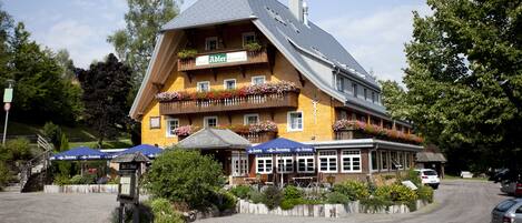 A two-story building with a sloped roof, a balcony with flower boxes, and a sign indicating it's a restaurant.