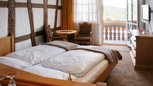 A hotel room with a large bed, a wooden desk, a chair, a small table, and a TV. - Hotel Adler Bärental (Feldberg)