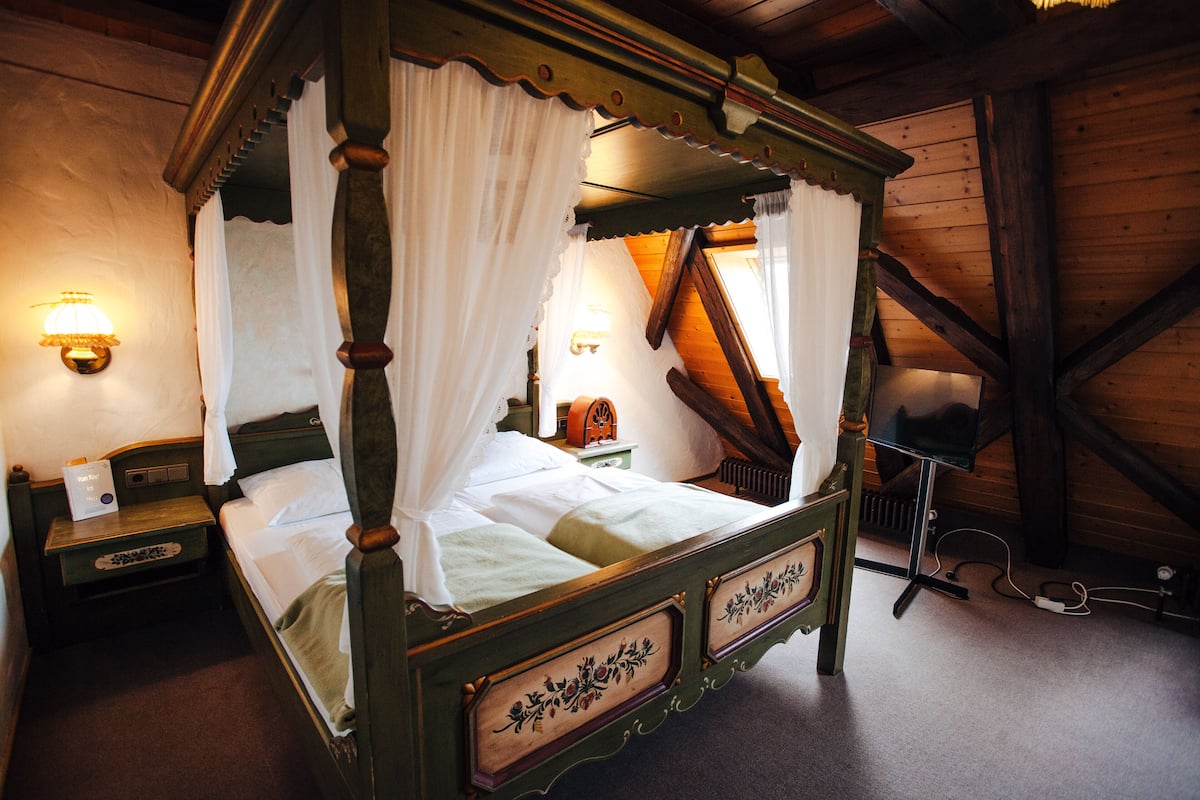 A four-poster bed with a canopy, a bedside table, a nightstand, and a lamp.