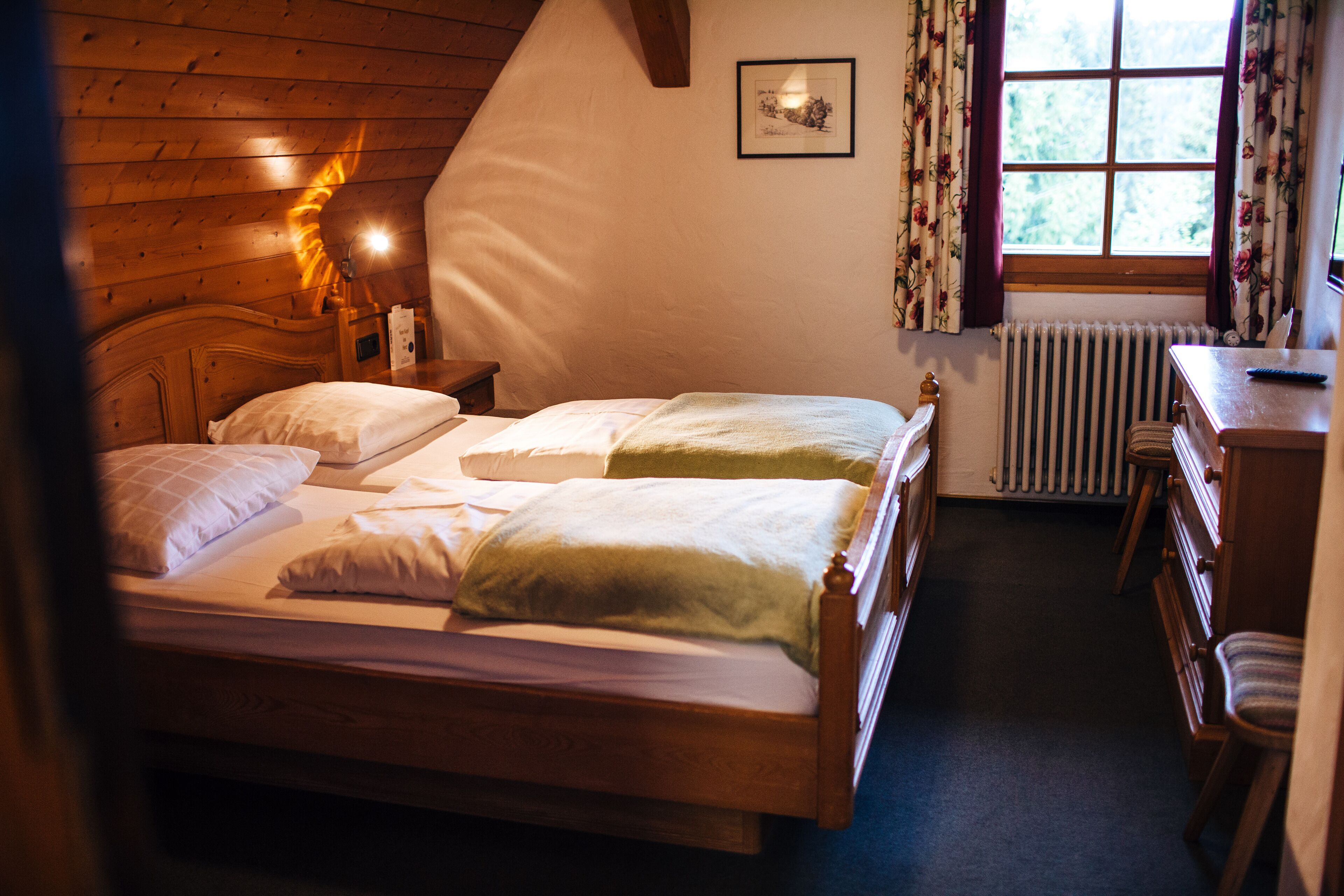 Un dormitorio acogedor con una cama de madera, una mesita de noche con lámpara, un radiador y una ventana con cortinas.
