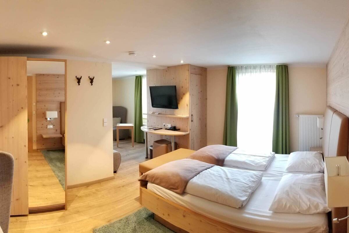 A modern hotel room with a wooden bed, a TV mounted on the wall, and a small desk with a chair.
