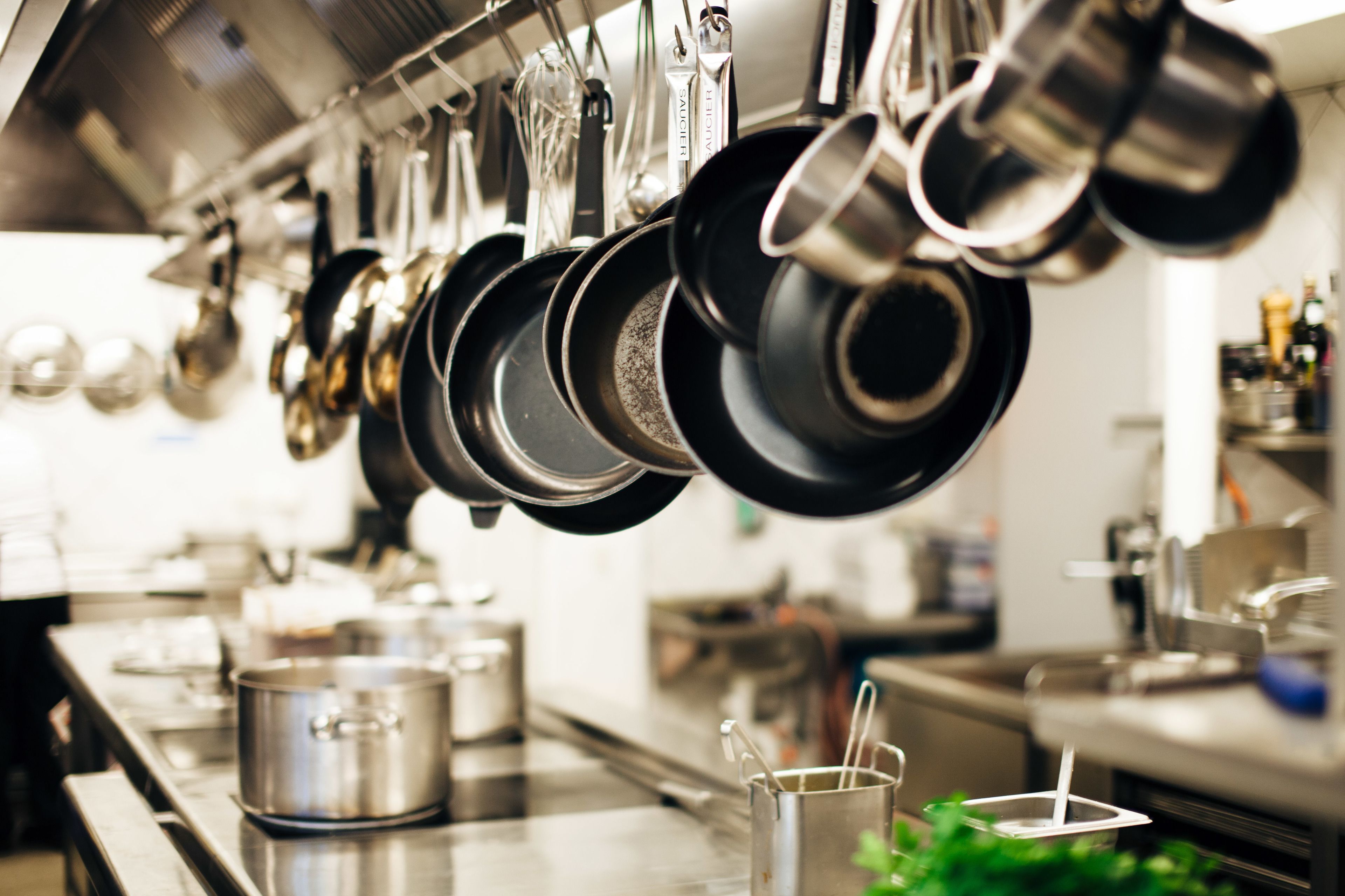 A kitchen with hanging pots and pans, stainless steel countertops, and a sink.