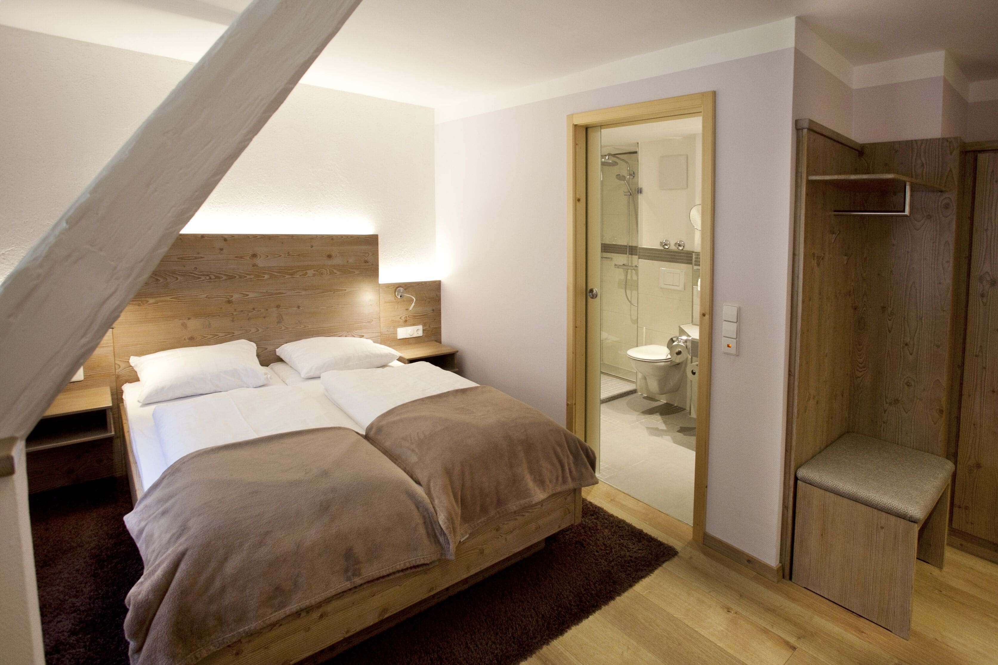 Une chambre à coucher avec un lit en bois, une table de chevet et une petite banquette en bois.