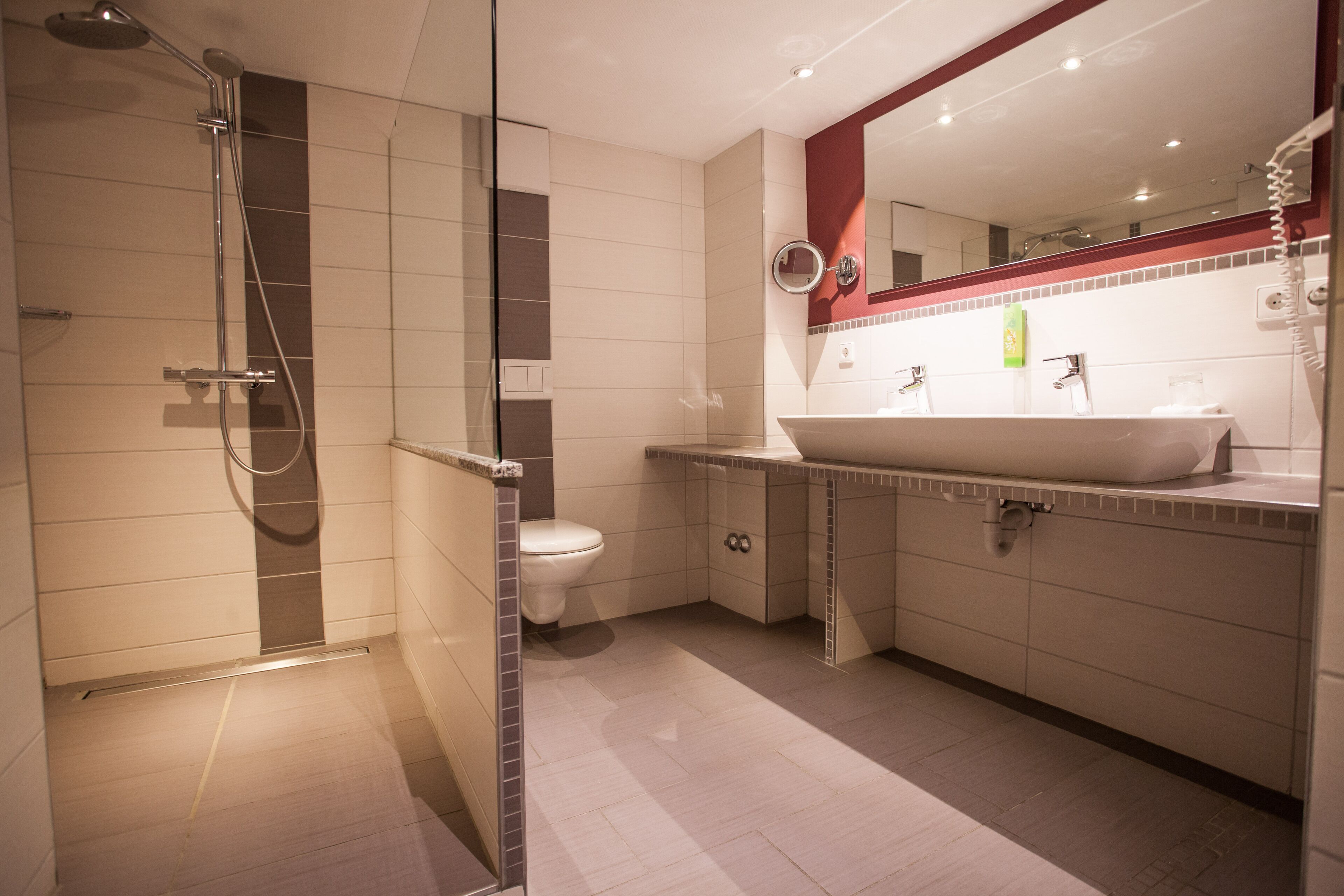 A modern bathroom with a glass-enclosed shower, a white toilet, and a vanity with a large mirror.