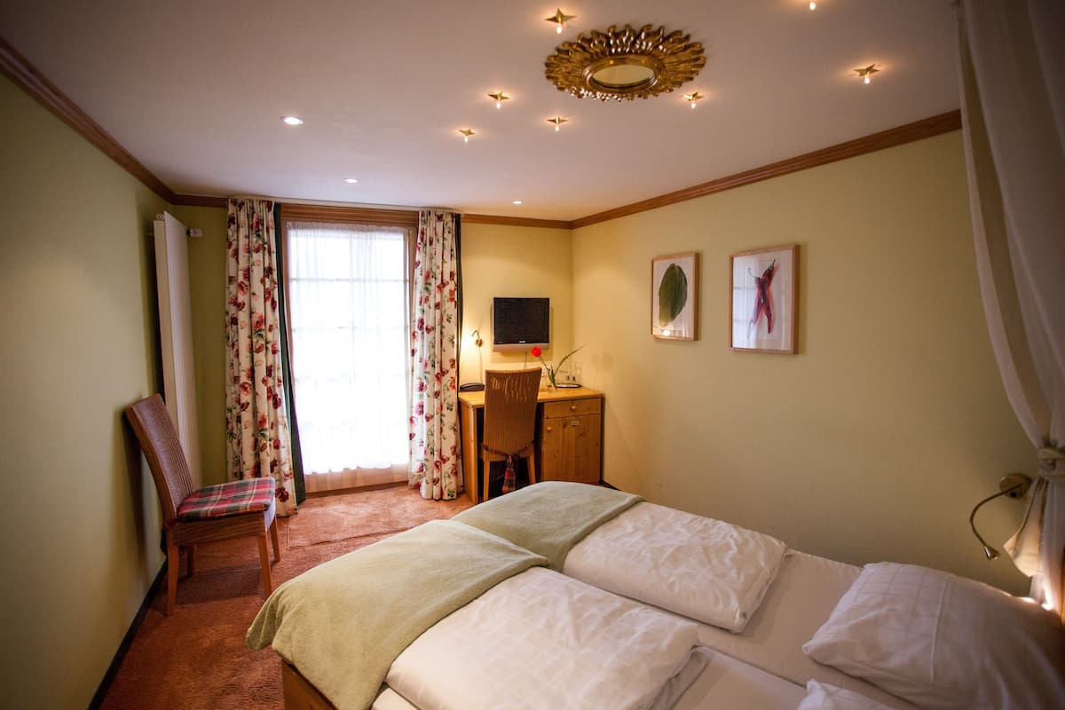 A hotel room with two beds, a desk with a chair, a television, and a window with curtains.