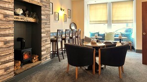 Una sala de estar acogedora con chimenea de piedra, un comedor con sillas y una mesa, y ventanas amplias con persianas.
