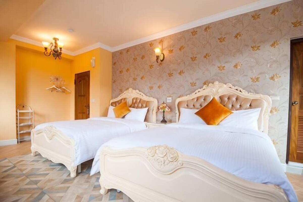 A hotel room with two beds, a chandelier, a wooden door, and patterned wallpaper.