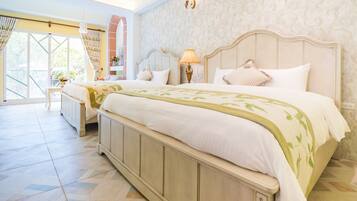 A spacious bedroom with a large bed, a nightstand, a lamp, and a view of the outdoors through a large window.