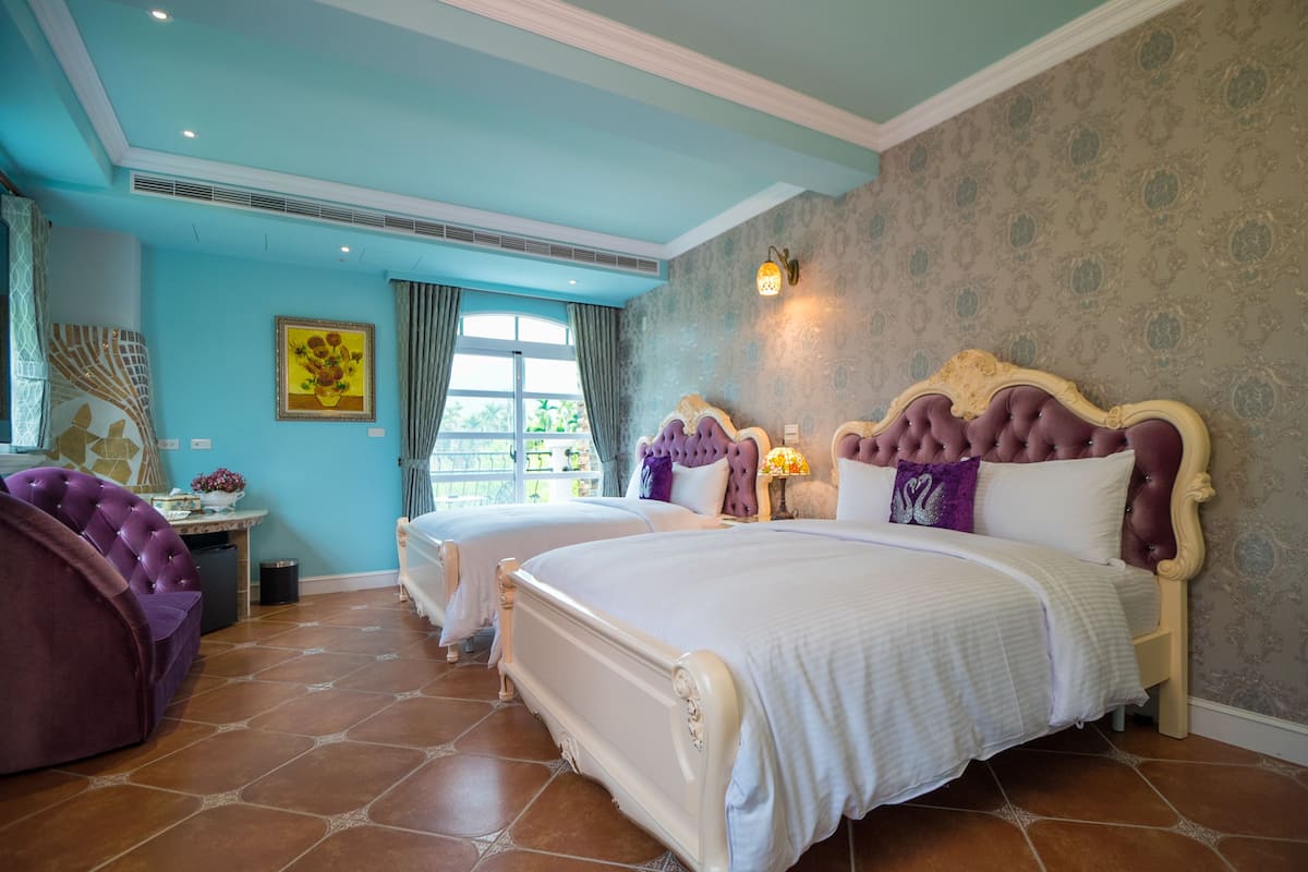 A bedroom with two beds, a vanity, and a window with curtains.