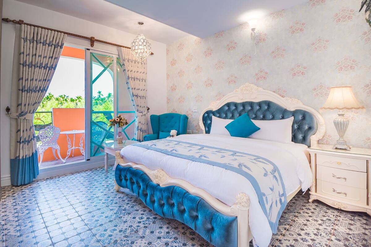 A bedroom with a large bed, a nightstand, a chair, and a view of the outdoors.