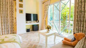 A room with a bed, a white table with a vase of flowers, a teddy bear, a TV, and a window with curtains. - Saint Paul Villa (Yuchi)