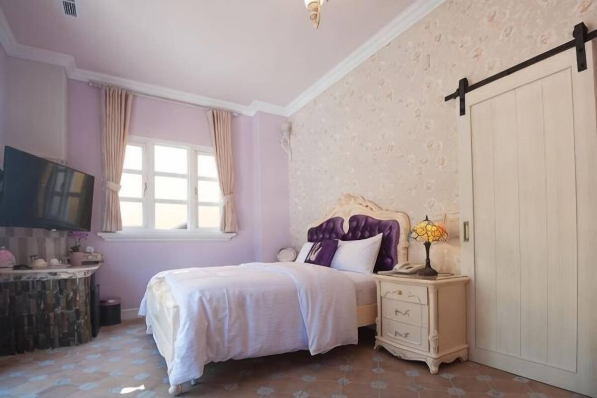A bedroom with a bed, dresser, vanity, and a sliding door.