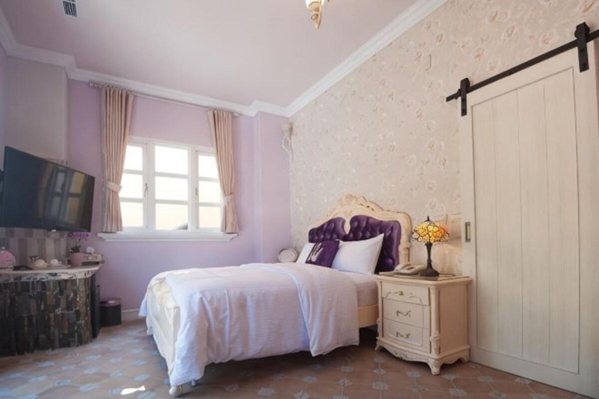 A bedroom with a bed, dresser, vanity, and a sliding door.