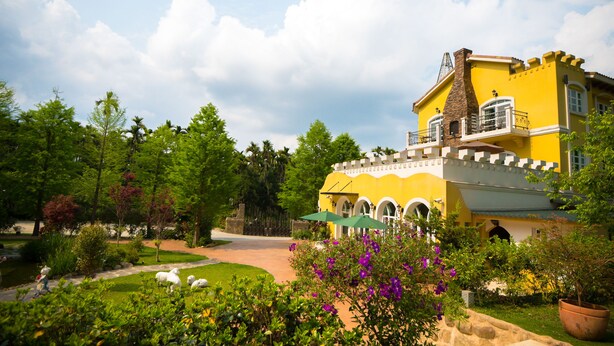 A yellow building with a castle-like facade, surrounded by lush greenery and a clear sky. - Saint Paul Villa (Yuchi)