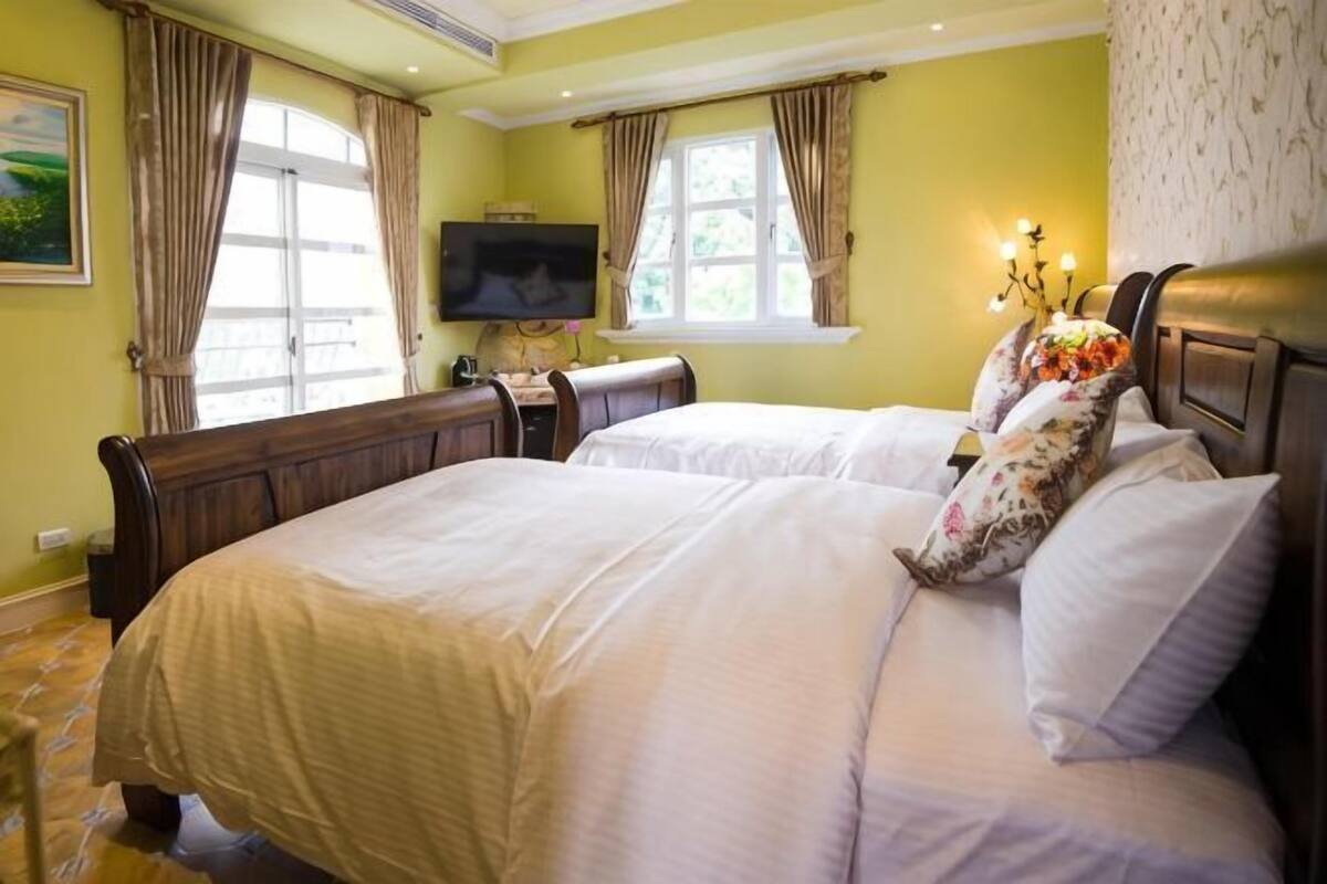 A bedroom with two beds, a television, and a window with curtains.