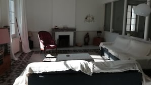 A living room with a fireplace, a red chair, a white sofa, and a large window. - Les Colonnades (Moussan)