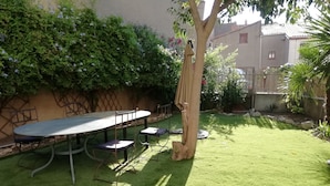 A patio with a round table and chairs, surrounded by a well-maintained lawn and a variety of plants. - Les Colonnades (Moussan)