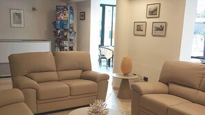 Ein stilvoller Lounge-Bereich mit beigen Sofas und einem Couchtisch in der Mitte. An den Wänden befinden sich gerahmte Bilder und im Hintergrund ein Bücherregal.
