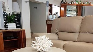 Ein Wohnzimmer mit einem beigen Sofa, einem runden Couchtisch mit einem dekorativen weißen Gegenstand und einem Fliesenboden mit geometrischem Muster.