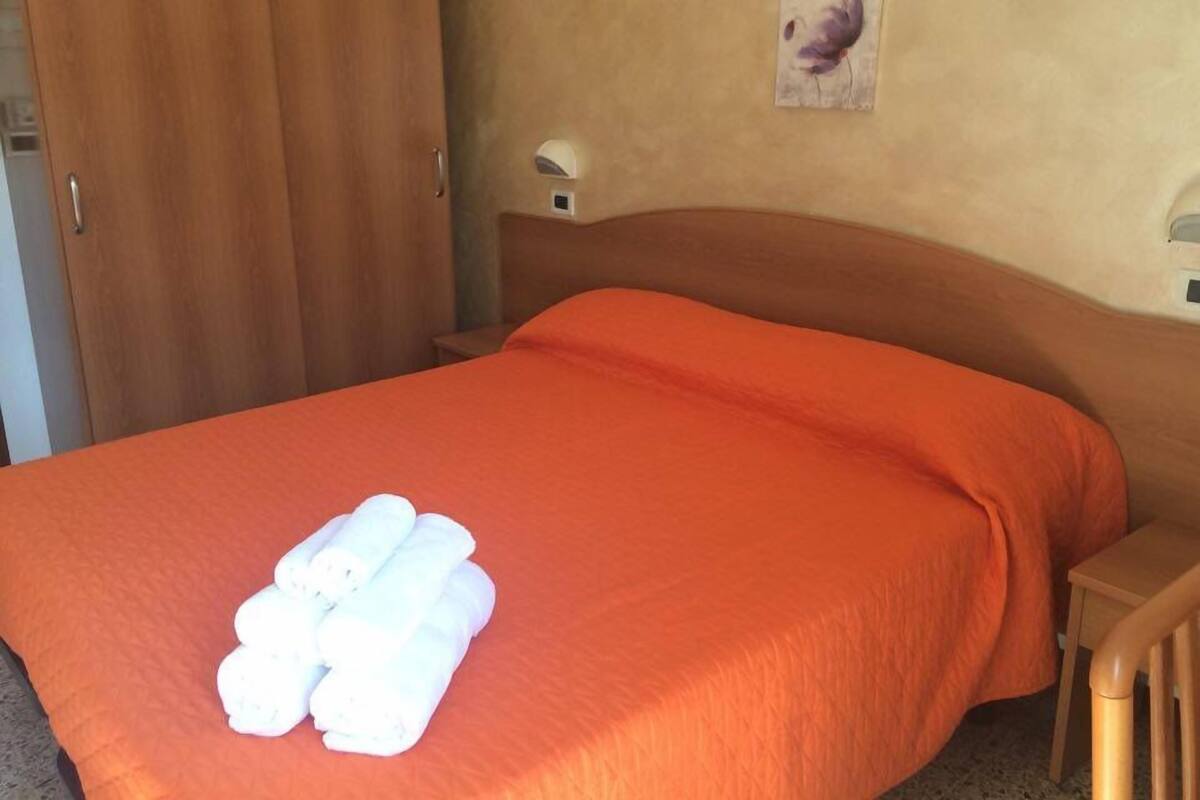 A hotel room with a bed, a wooden headboard, a wall-mounted light, and a door.