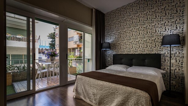A bedroom with a large bed, a patterned wall, and a view of an outdoor patio. - Residenza Gregorio VII (Rome)