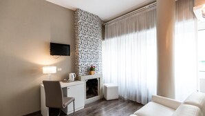 A modern living room with a fireplace, a flat-screen TV mounted on the wall, a white sofa, and a desk with a chair. - Residenza Gregorio VII (Rome)