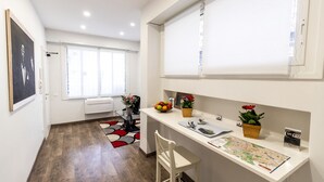 A modern kitchen with a white countertop, a dining area with a chair, a window with blinds, and a WiFi sign. - Residenza Gregorio VII (Rome)