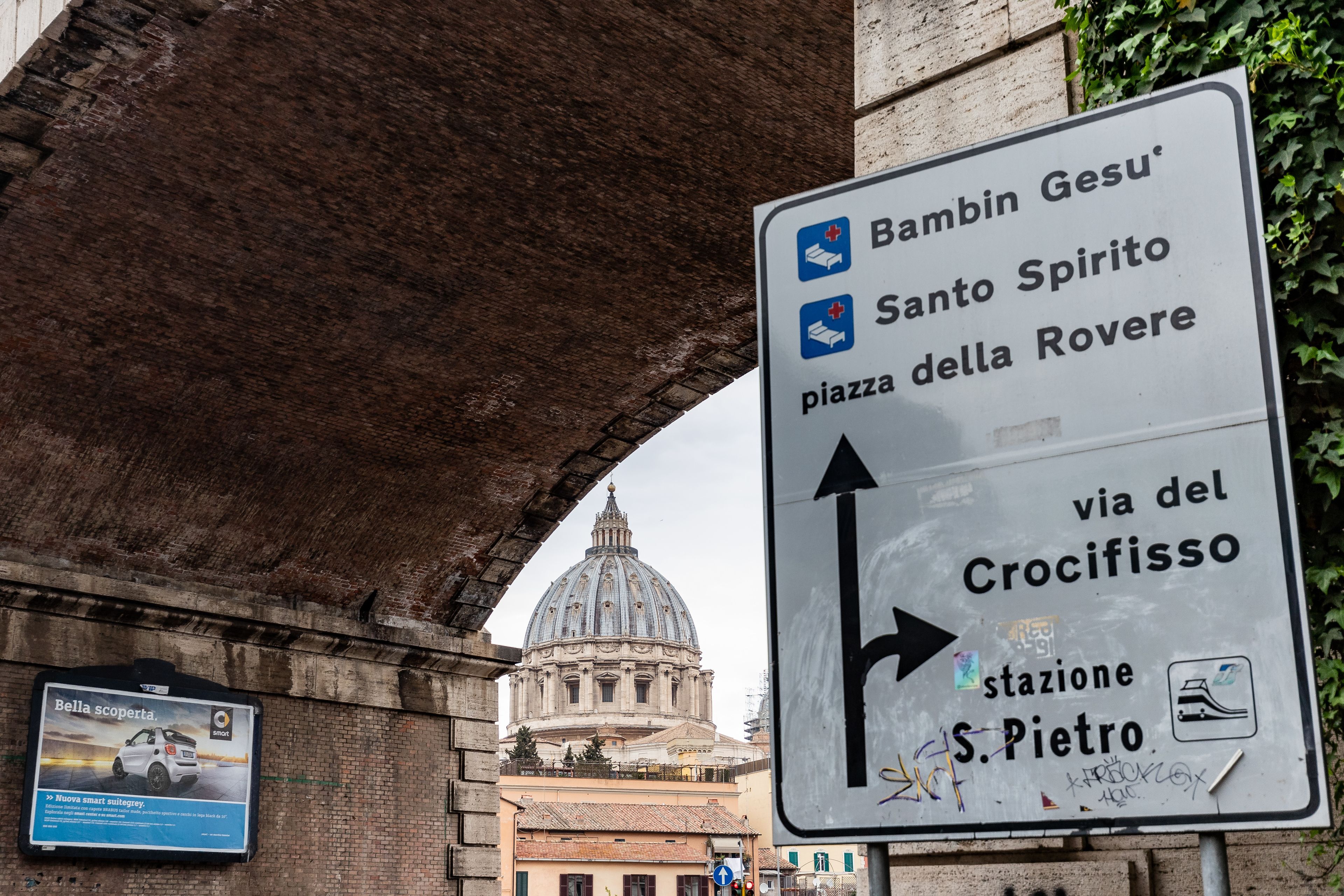 Un panneau de signalisation indiquant la direction à suivre grâce à des flèches pointant vers des points de repère tels que Bambin Gesu, Santo Spirito et la place della Rovere, et mentionnant la station S. Pietro, via del Crocifisso.