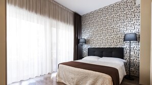 A hotel room with a large bed, a patterned wall, and two floor lamps. - Residenza Gregorio VII (Rome)