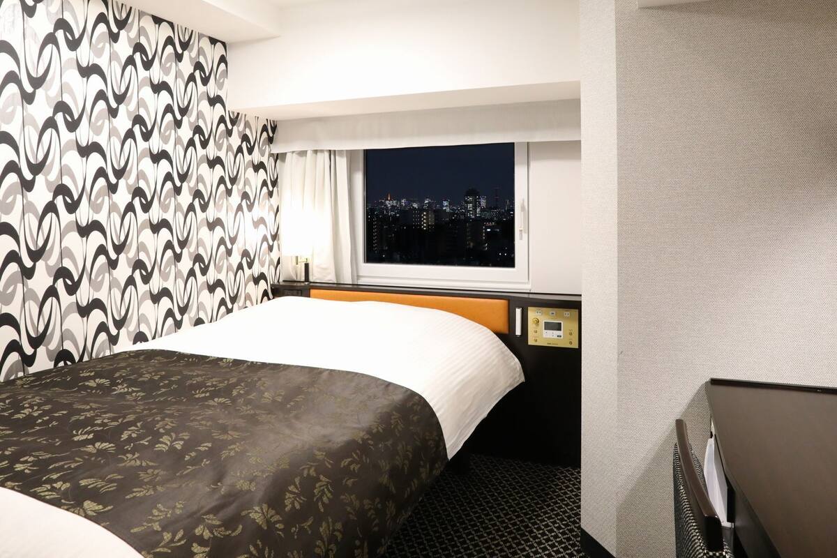 Une chambre d’hôtel avec un lit, une fenêtre donnant sur la ville, une table de chevet et un miroir.