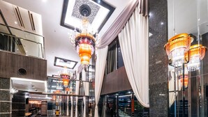 Un hall d’entrée spacieux, doté d’un plafond haut, de lustres, de surfaces réfléchissantes et d’espaces aménagés pour s’asseoir.