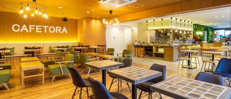 A modern cafe interior with wooden flooring, green and black chairs, and a visible kitchen area.