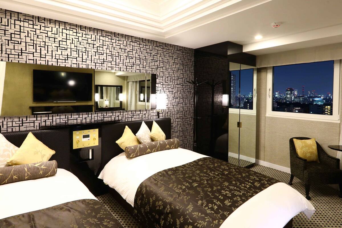 Ein Hotelzimmer mit modernem Design, das ein großes Bett mit gemusterten Textilien, einen Flachbildfernseher, einen Spiegel und einen Blick auf die Stadt durch ein Fenster bietet.