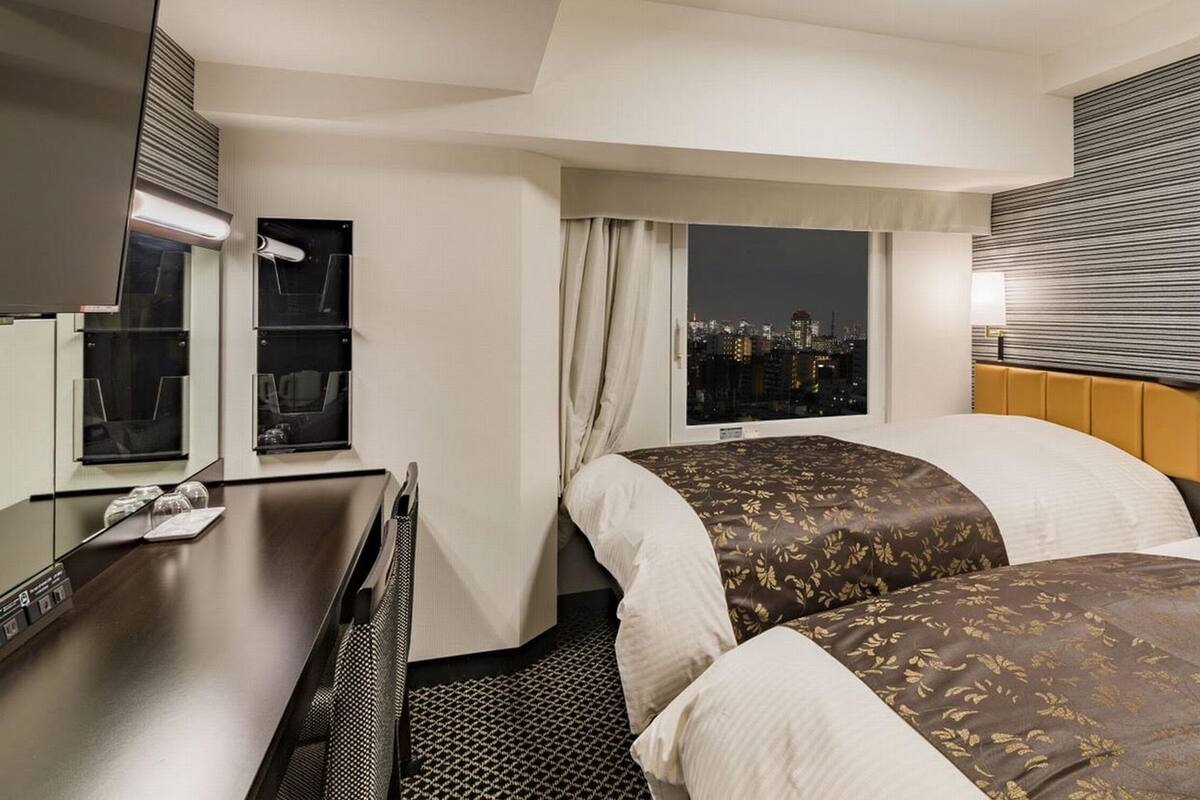 Une chambre d’hôtel avec deux lits, un bureau, une fenêtre donnant sur la ville et un panneau de commande sur la tête de lit.