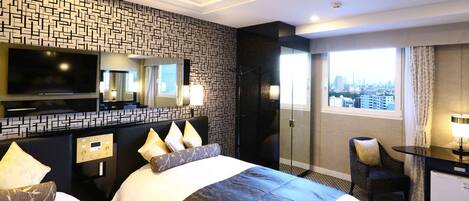 A hotel room with a large bed, a TV, a desk with a lamp, and a city view.