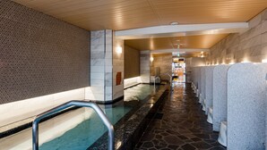 Un espace spa moderne avec un sol carrelé en pierre, un long banc et une rangée d’éviers en pierre.